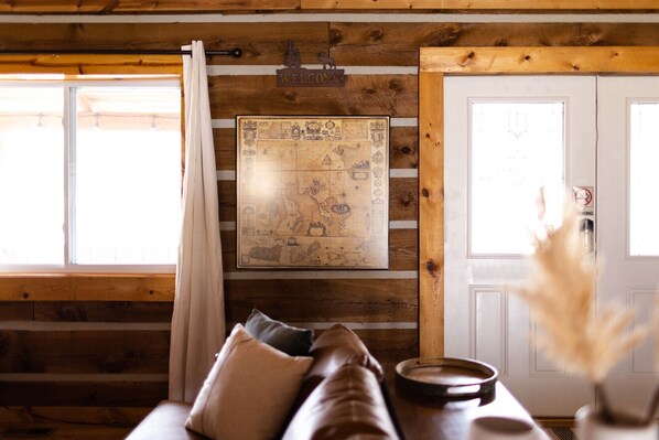 A cozy cabin interior with a wooden wall, a map, a couch, and a door with a 'No Smoking' sign.