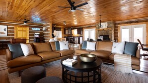 Un intérieur de chalet chaleureux avec un plafond en bois, un grand ensemble de canapés, un coin repas et une cuisine.