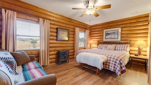A log cabin bedroom with a bed, a sofa, a small heater, and a ceiling fan. - Cozy Custom Cabin In The Pines-Williams AZ (Williams)