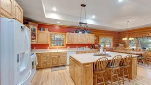A spacious kitchen with wooden cabinets, a central island with chairs, and a hanging light fixture. - Cozy Custom Cabin In The Pines-Williams AZ (Williams)