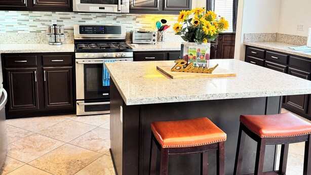 A modern kitchen with dark wood cabinets, stainless steel appliances, a granite countertop, and a central island with stools. - Peaceful Home Away! (San Jacinto)