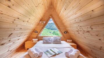 Une pièce chaleureuse en bois, avec un lit, des oreillers et des serviettes, une fenêtre donnant sur un paysage verdoyant et une petite table de chevet.