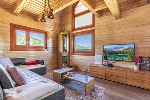 L’intérieur chaleureux d’un chalet avec un canapé, une table basse et un téléviseur fixé à un mur en bois.