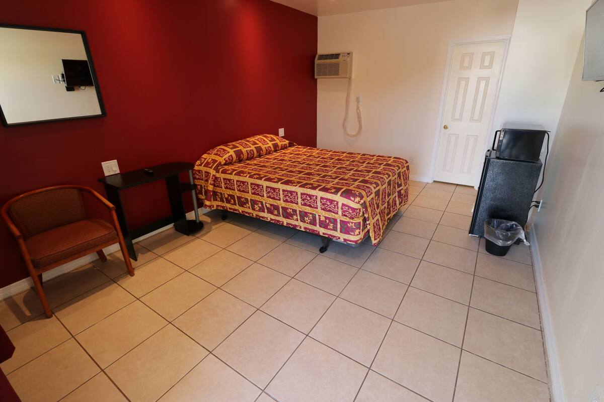 A room with a bed, a chair, a desk, and a trash bin.