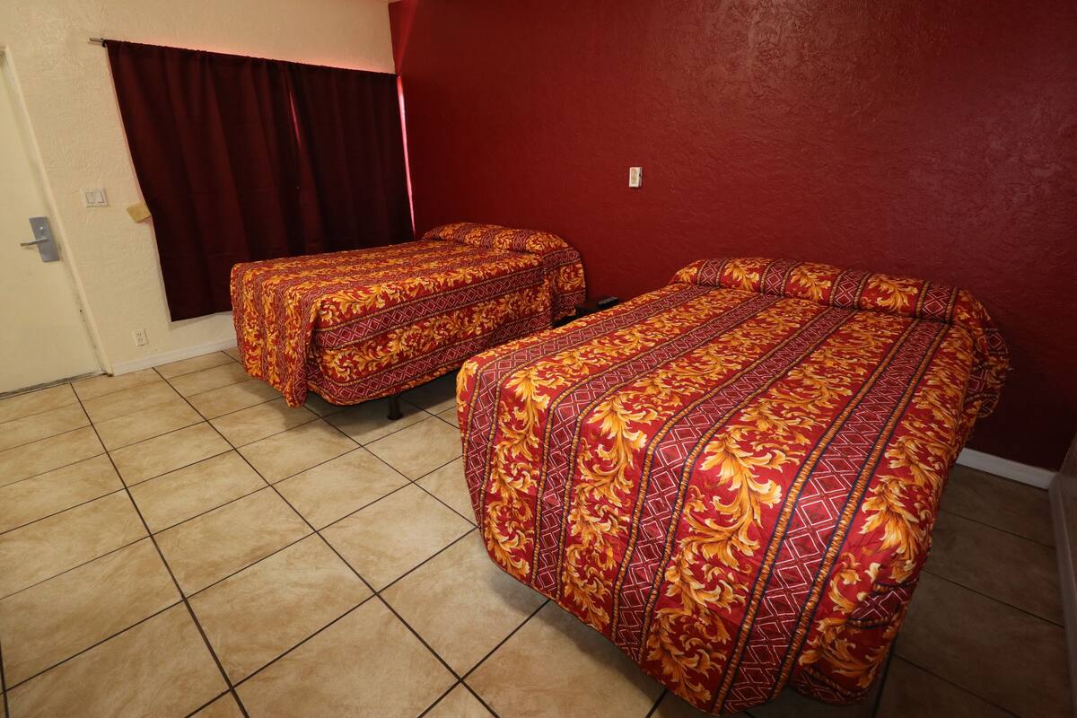 A room with two beds, each with patterned bedding, a red wall, and a tiled floor.