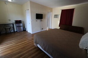 A bedroom with a bed, a desk with a microwave, a television, and a door. - Sandman Inn Motel (Daytona Beach)
