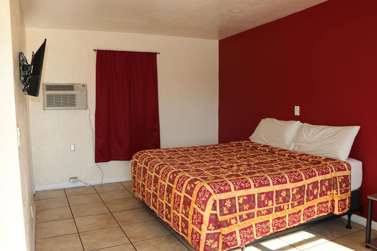 A bedroom with a red wall, a bed with white linens, a red curtain, and an air conditioning unit on the wall.