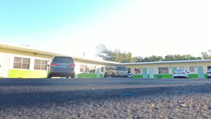 Ein Motel mit einer Reihe von Zimmern, einem Parkplatz und einem Gebäude mit einer grün-weißen Fassade.