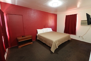 A room with a bed, a wooden dresser, a television mounted on the wall, and a window with red curtains. - Sandman Inn Motel (Daytona Beach)