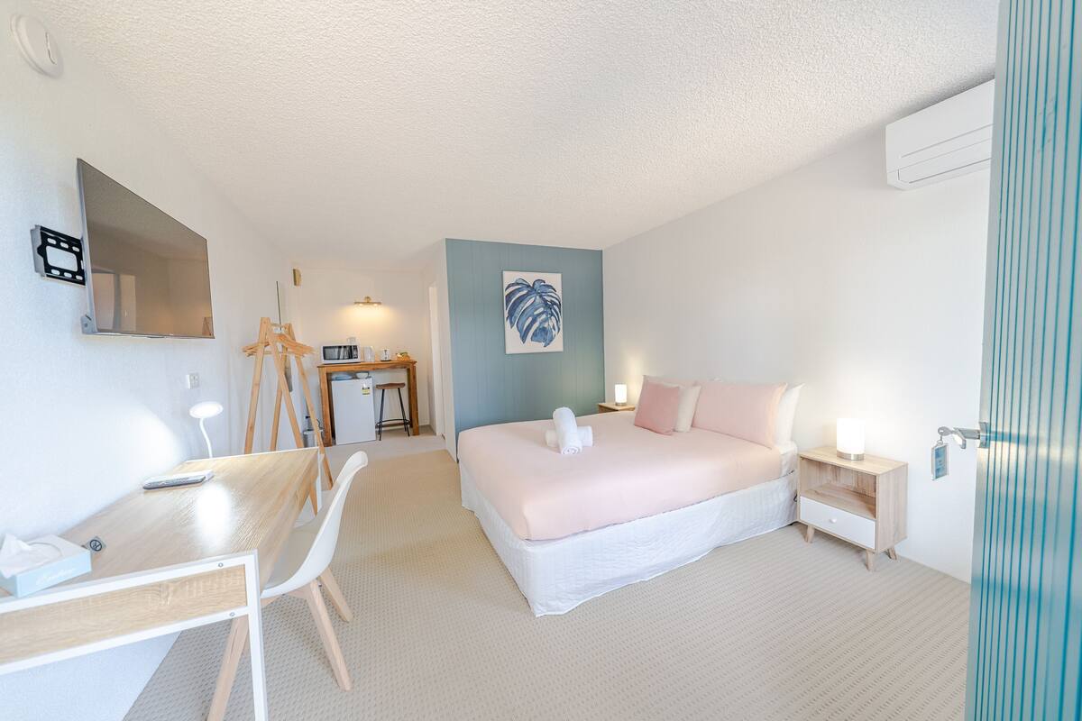 Ein Schlafzimmer mit Bett, Nachttisch, Schreibtisch, Stuhl und einem wandmontierten Spiegel.