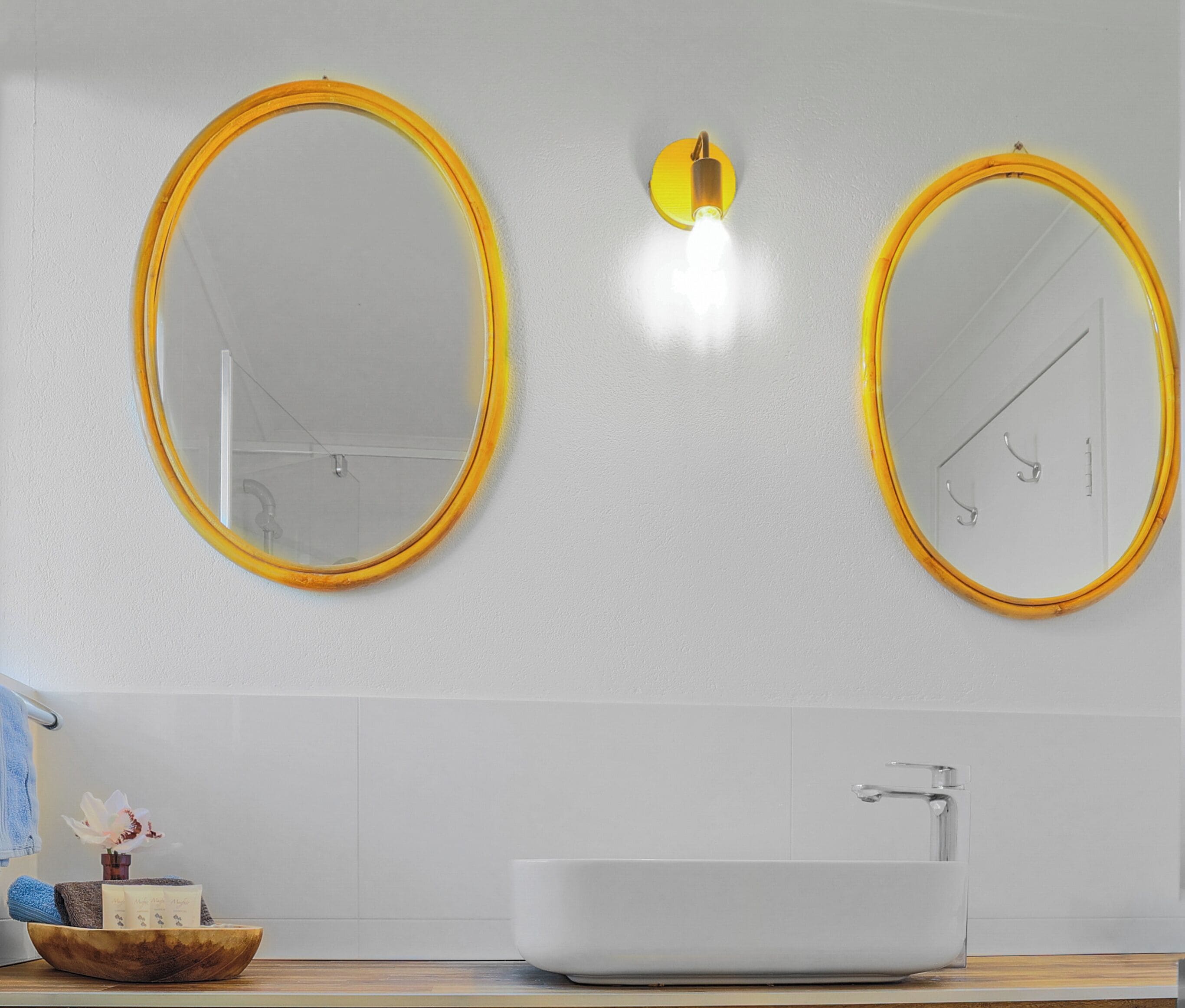 A bathroom with two oval mirrors, a white sink, and a towel rack.