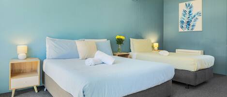 Habitación de hotel con dos camas, una mesita de noche con lámpara, un florero con flores y un cuadro en la pared.