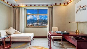 A hotel room with a bed, a desk, a chair, and a view of mountains through a large window.