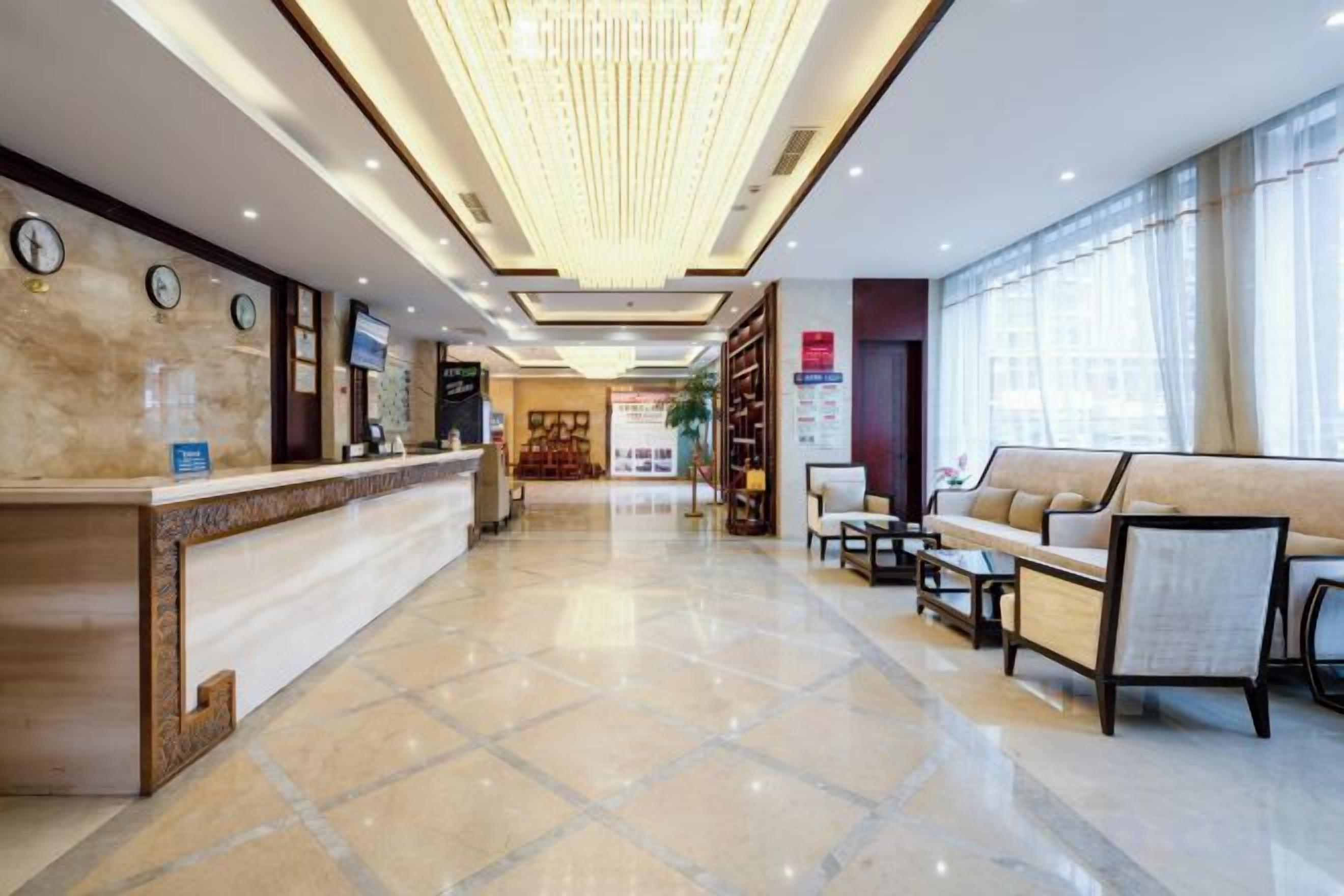 A hotel lobby with a reception desk, seating area, and a chandelier.