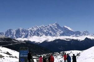 A group of people on a snowy mountain with a clear sky and a signboard.