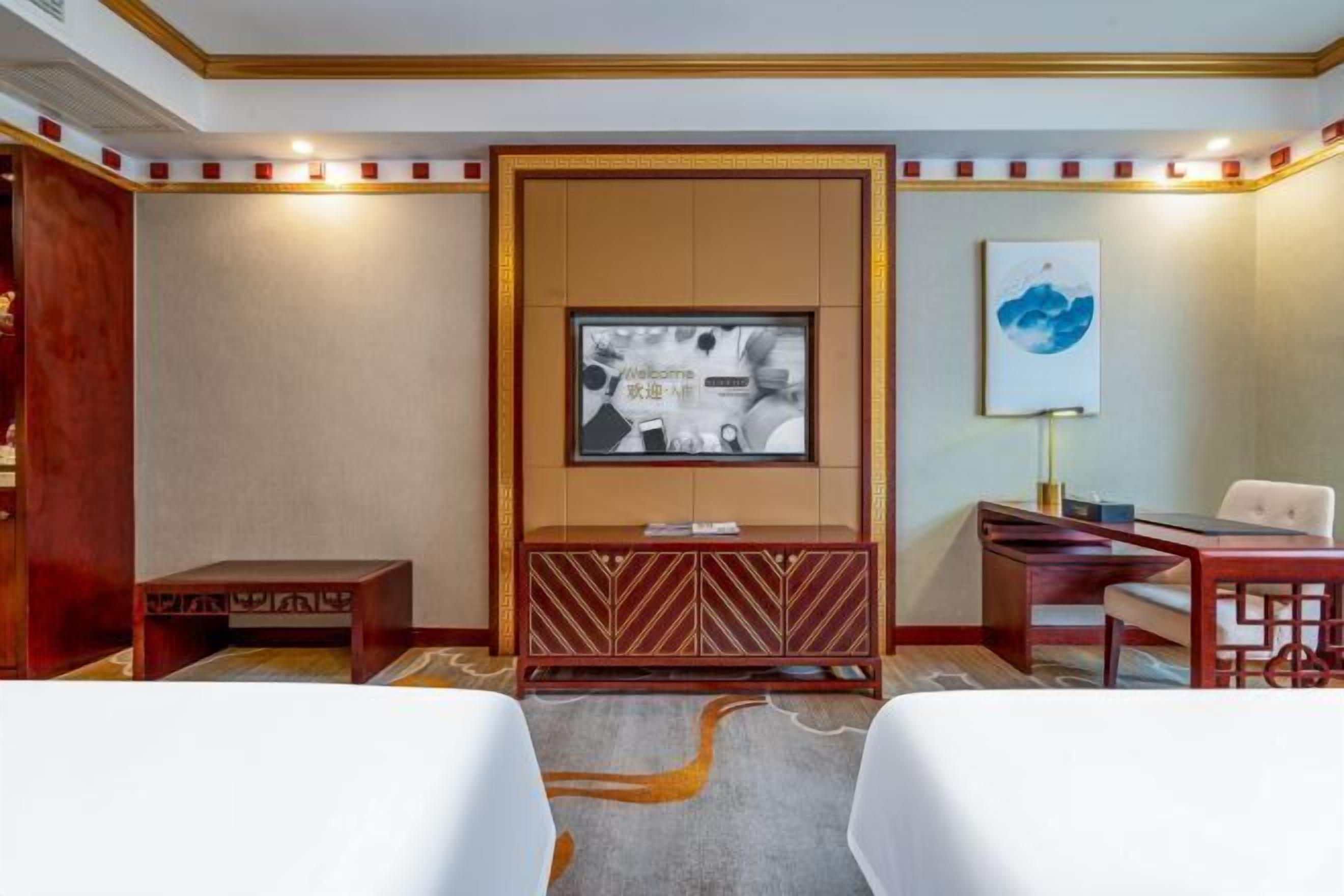 Ein Hotelzimmer mit Holzschrank, Wandfernseher, Schreibtisch mit Stuhl und einem kleinen Tisch.