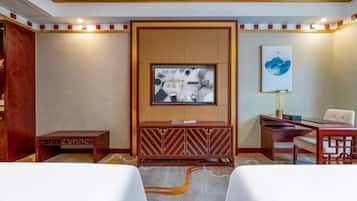 Ein Hotelzimmer mit Holzschrank, Wandfernseher, Schreibtisch mit Stuhl und einem kleinen Tisch.