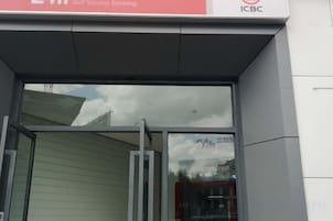 Entrada de un banco con puerta de vidrio y letrero indicando servicios bancarios sin asistencia.