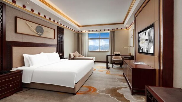 A hotel room with a large bed, a desk, a TV, and a window with a mountain view.