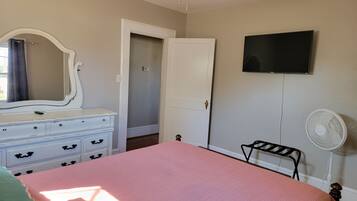 Een slaapkamer met een bed, een dressoir, een spiegel, een plafondventilator, een televisie en een deur naar een andere kamer.