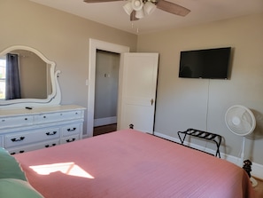 A bedroom with a bed, dresser, mirror, ceiling fan, TV, and a door leading to another room. - Cozy Fayetteville Home - King Bed - Sleeps 5 - Near Downtown (Fayetteville)