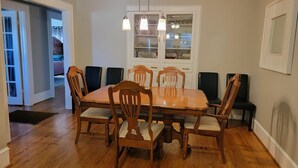 Een eetkamer met een houten tafel en stoelen, een kroonluchter en een kast met glazen deuren.