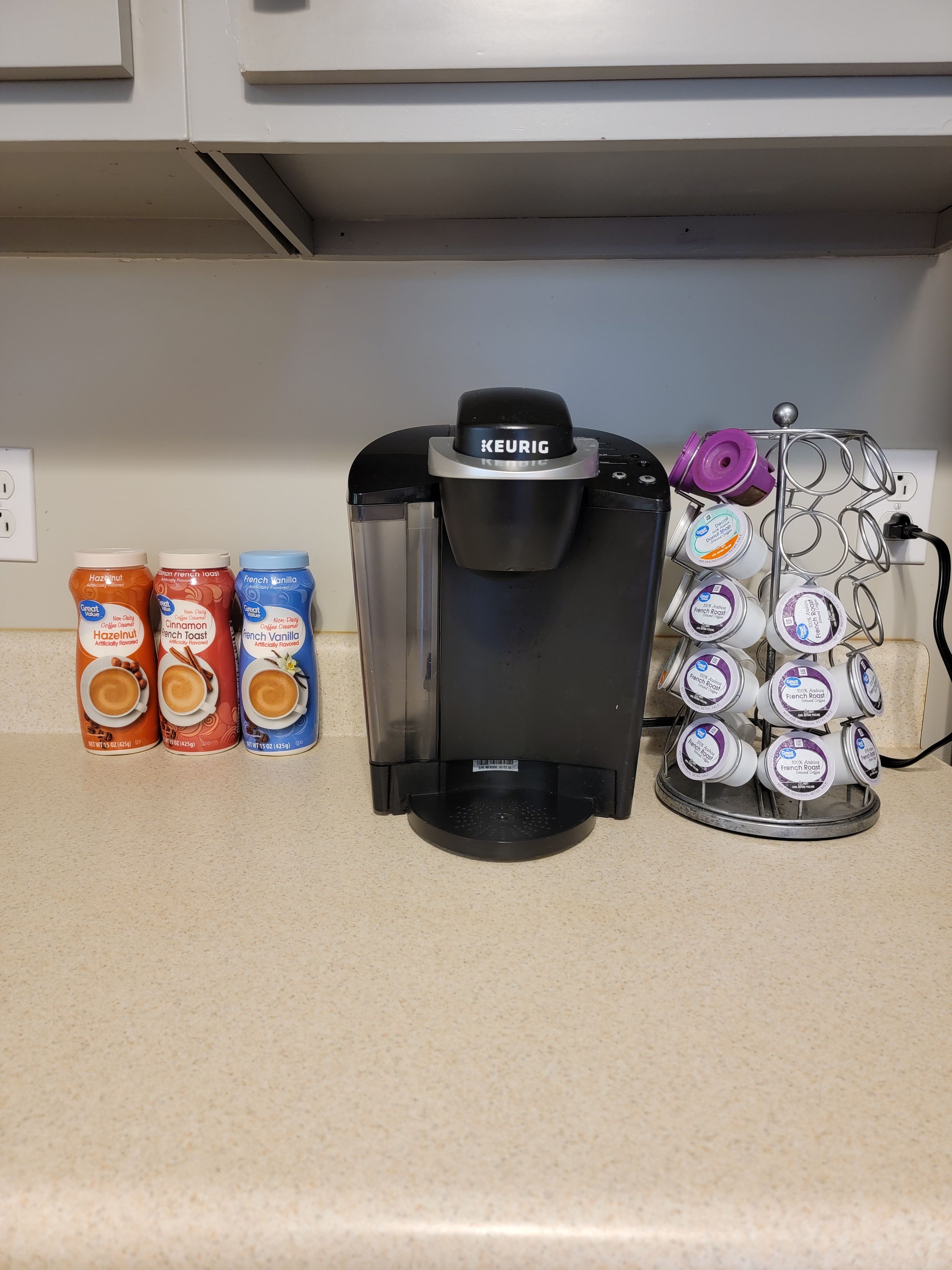 Een Keurig koffiezetapparaat op een aanrecht, met drie koffiecups en een houder voor koffiecups.