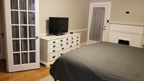 A bedroom with a bed, a dresser with drawers, a television on top, a fireplace, and a door with curtains. - Clean and spacious house in downtown Fayetteville (Fayetteville)