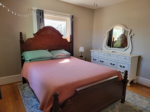 A bedroom with a wooden bed, a dresser, a mirror, and a window with curtains. - Cozy Fayetteville Home - King Bed - Sleeps 5 - Near Downtown (Fayetteville)