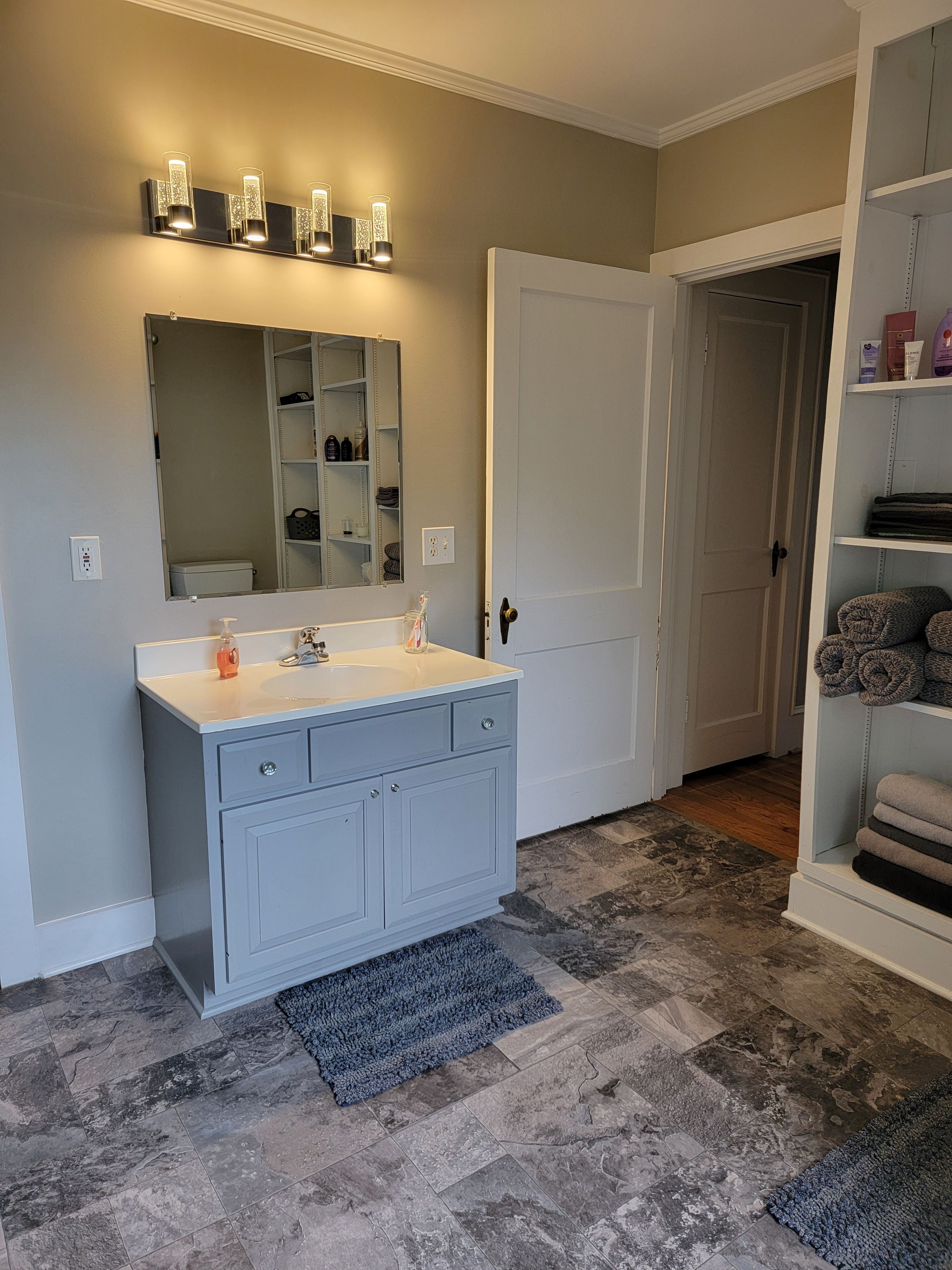 A bathroom with a vanity, a mirror, a towel rack, and a door leading to another room.