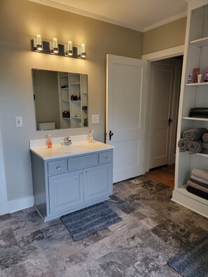 A bathroom with a vanity, a mirror, a towel rack, and a door leading to another room. - Cozy Fayetteville Home - King Bed - Sleeps 5 - Near Downtown (Fayetteville)
