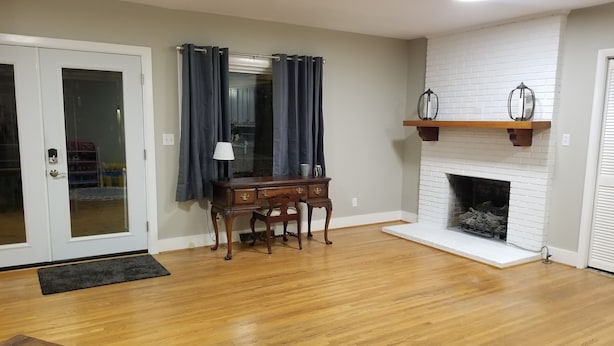 A living room with a wooden floor, a desk with drawers, a chair, a fireplace, and a door with glass panels. - Clean and spacious house in downtown Fayetteville (Fayetteville)