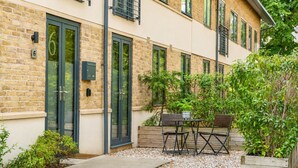 A modern building with a brick facade, numbered 6, featuring a patio with outdoor furniture and greenery.