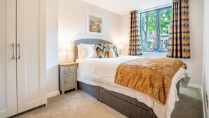 Ein Schlafzimmer mit einem Bett, Nachttischen, einer Lampe, einem Gemälde und Blick ins Freie.