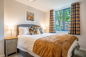 Ein Schlafzimmer mit einem Bett, zwei Nachttischlampen, einem Nachttisch, einem Fenster mit Vorhängen und einem Bild an der Wand.