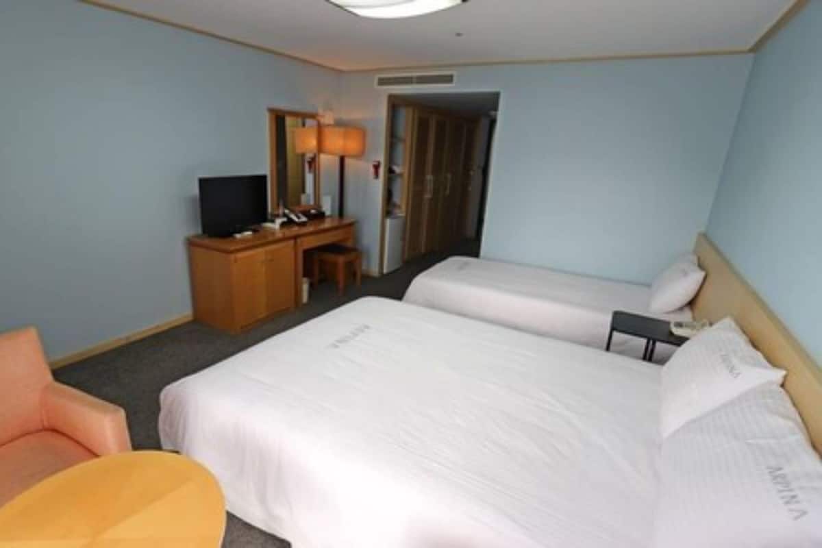 A hotel room with two beds, a desk, a chair, and a television.