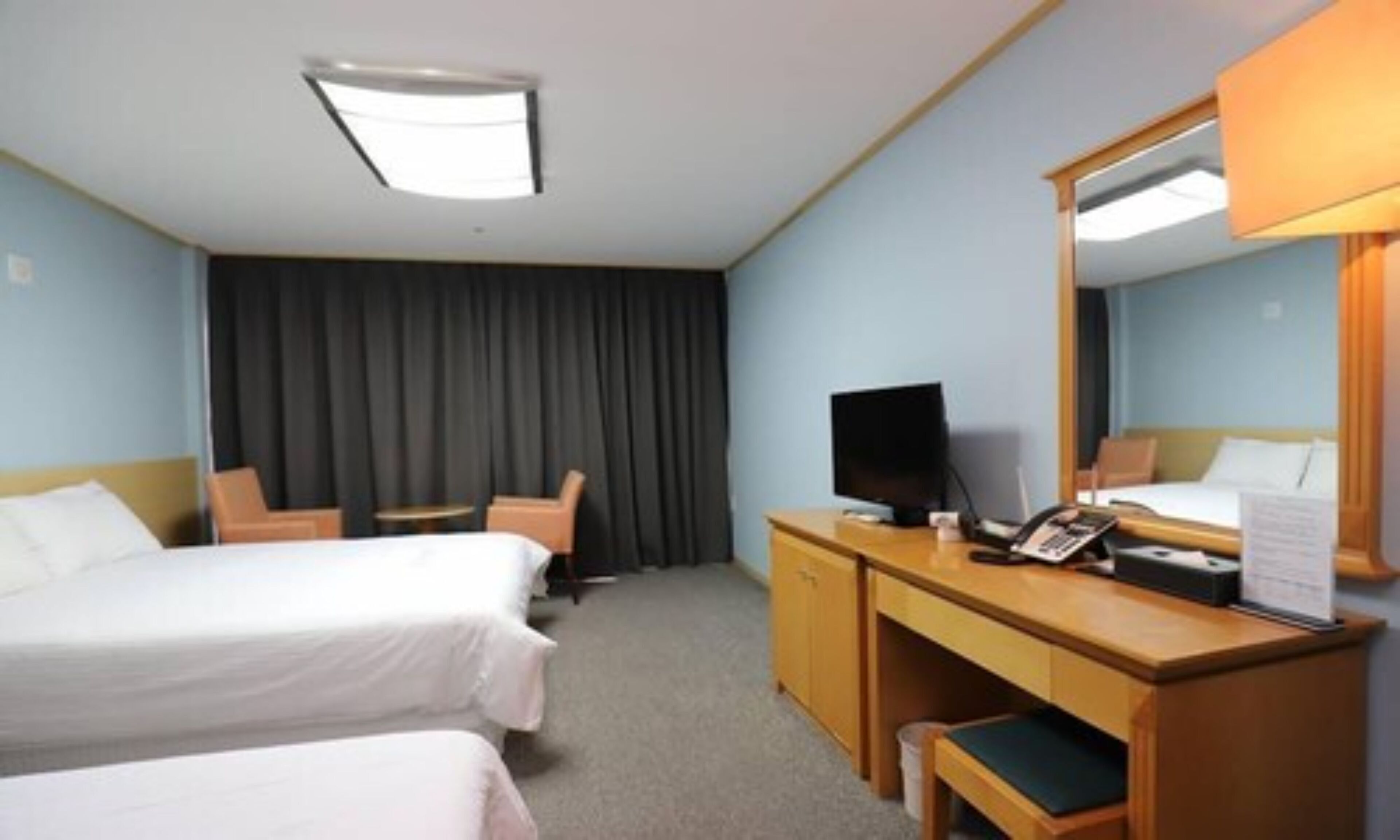A hotel room with two beds, a desk with a computer, a chair, and a large mirror.