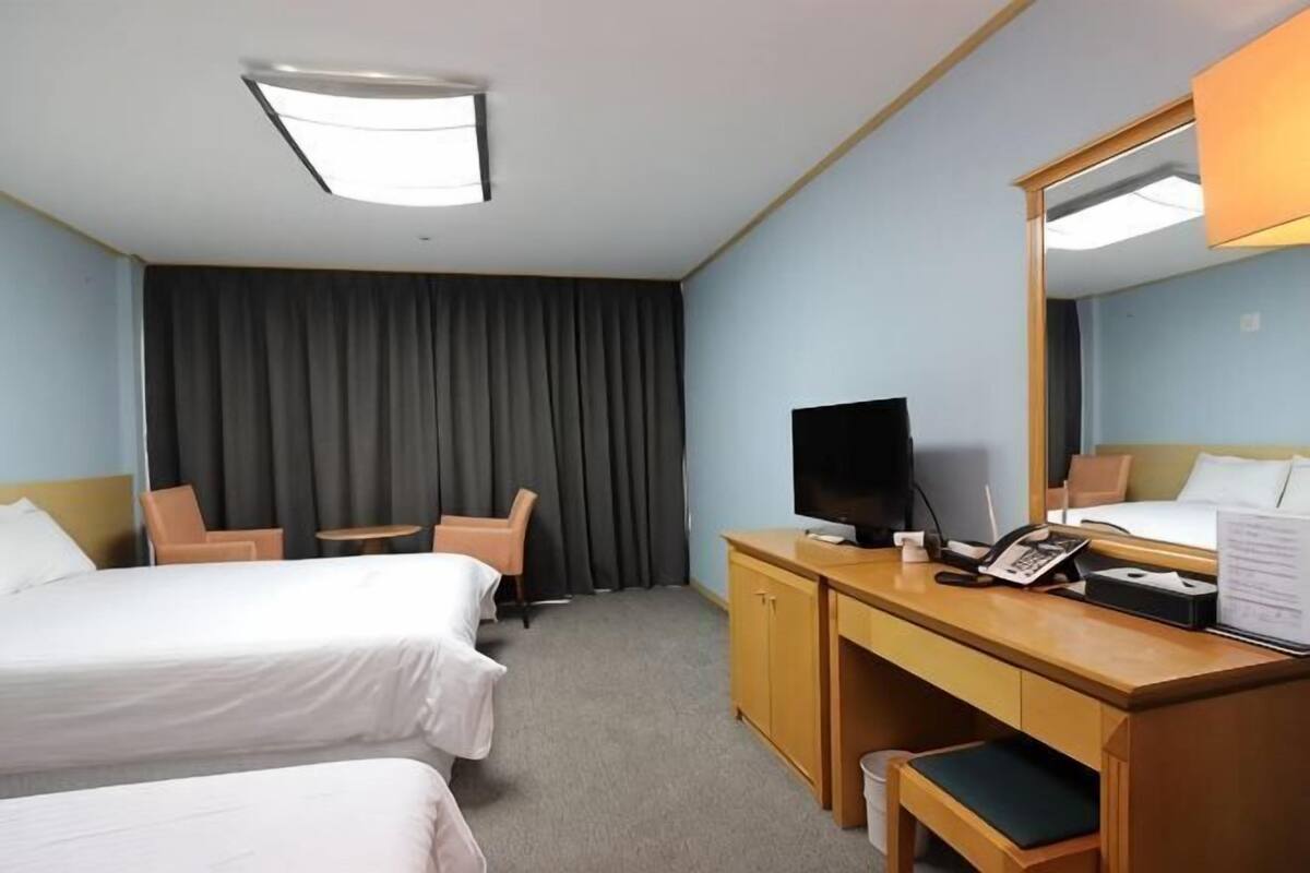 A hotel room with two beds, a desk with a computer, a television, and a large mirror.