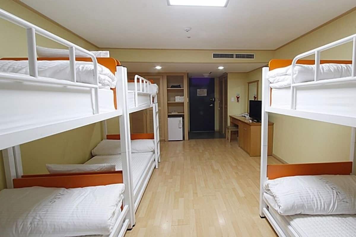 A dormitory room with bunk beds, a desk, a television, and a small refrigerator.