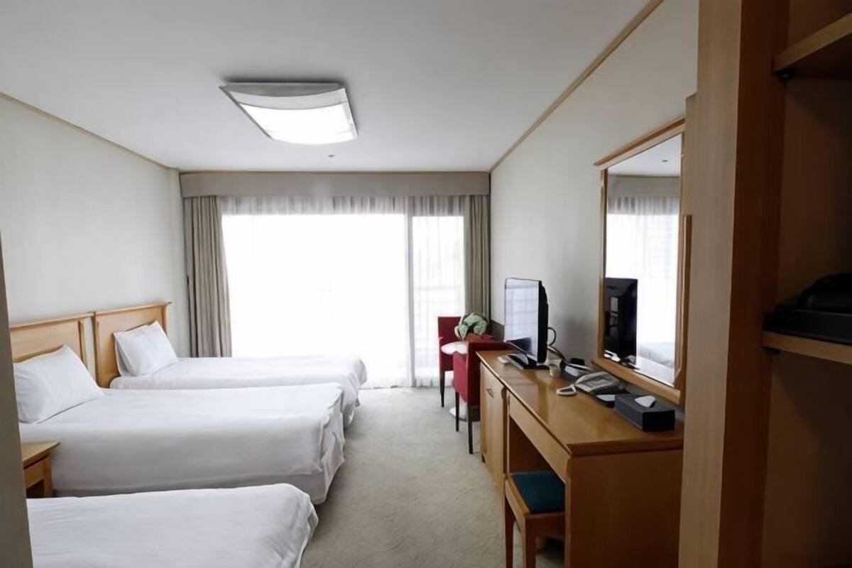 A hotel room with two beds, a desk, a chair, a television, and a large mirror.