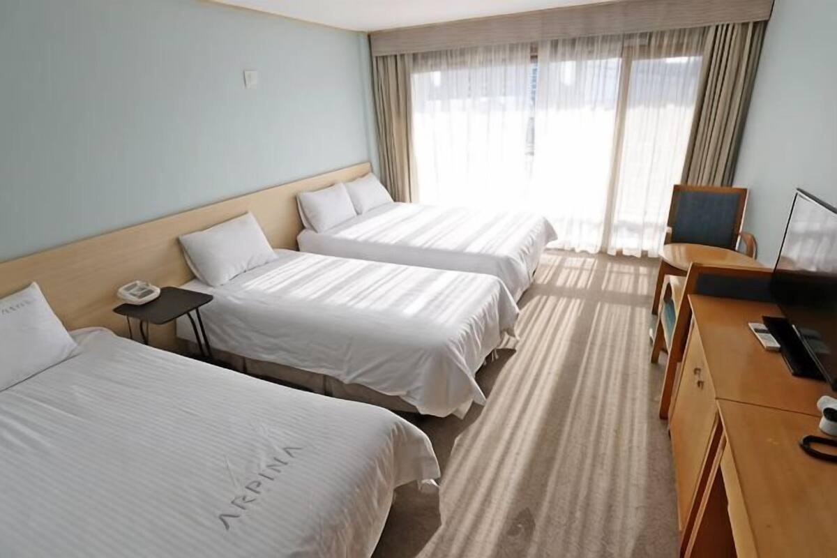 A hotel room with three beds, a desk, a chair, and a TV.