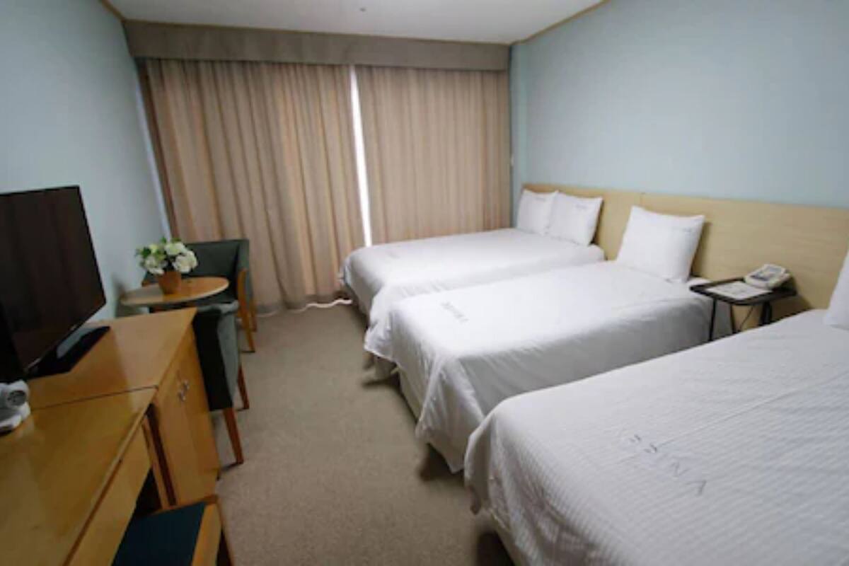 A hotel room with two beds, a desk with a chair, a television, and a window with curtains.