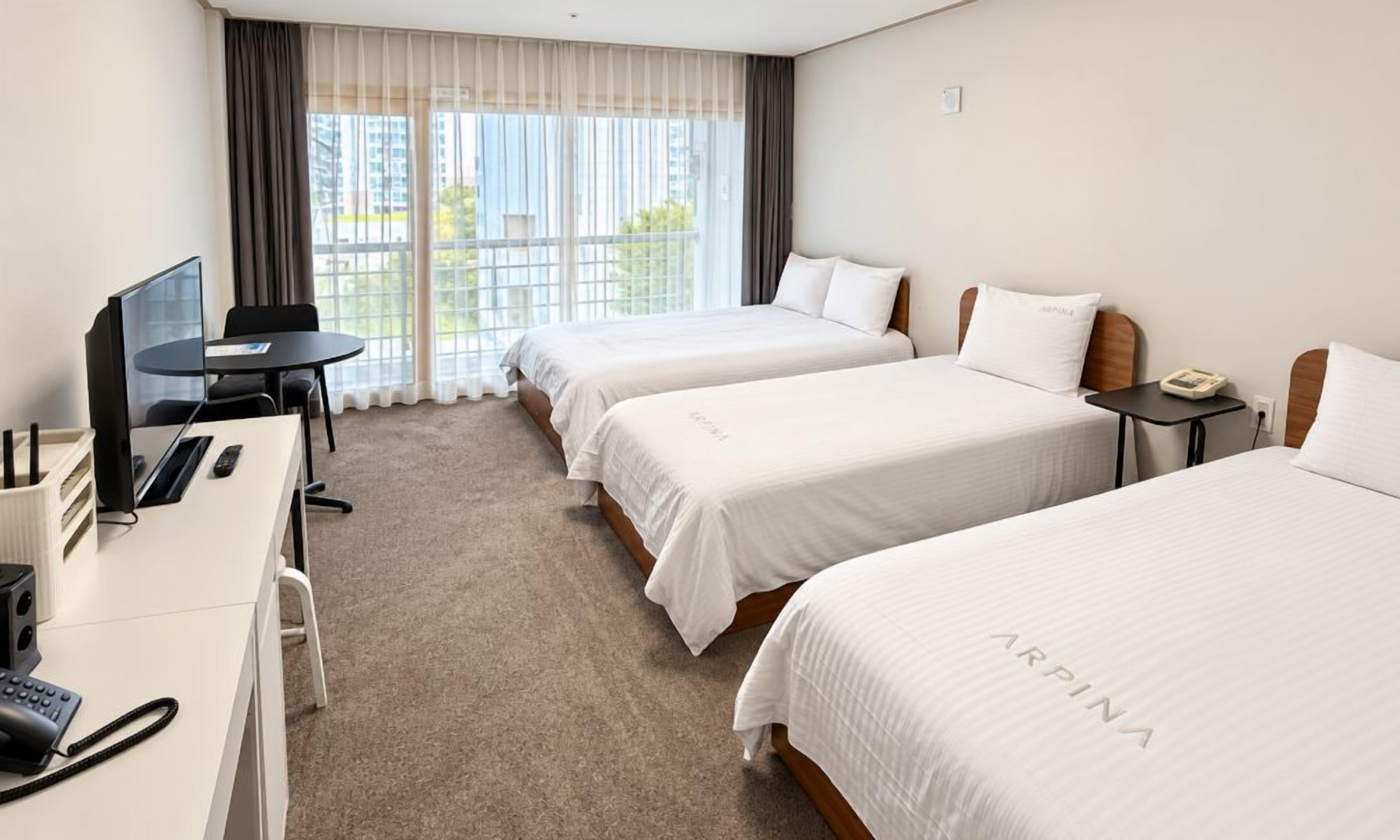 Quarto de hotel com duas camas, uma escrivaninha com computador, telefone e janela com cortinas.