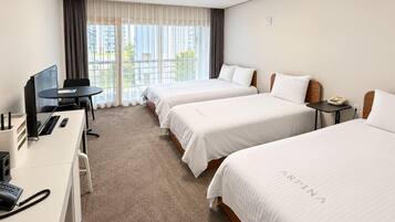 Quarto de hotel com duas camas, uma escrivaninha com computador, telefone e janela com cortinas.