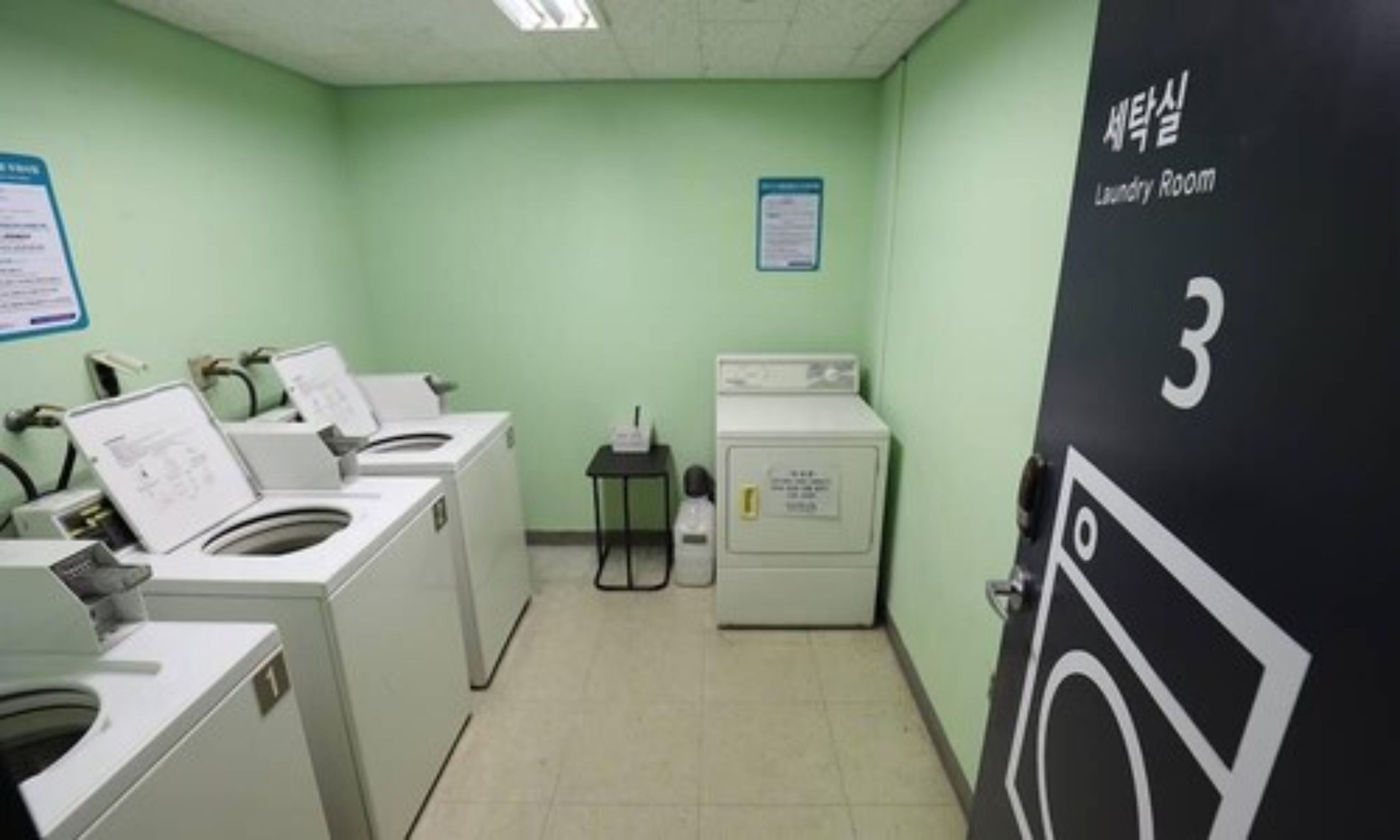 A laundry room with two washing machines, a dryer, and a small table with a bottle.