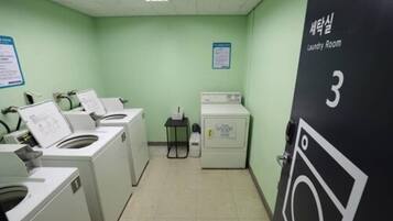 A laundry room with two washing machines, a dryer, and a small table with a bottle.