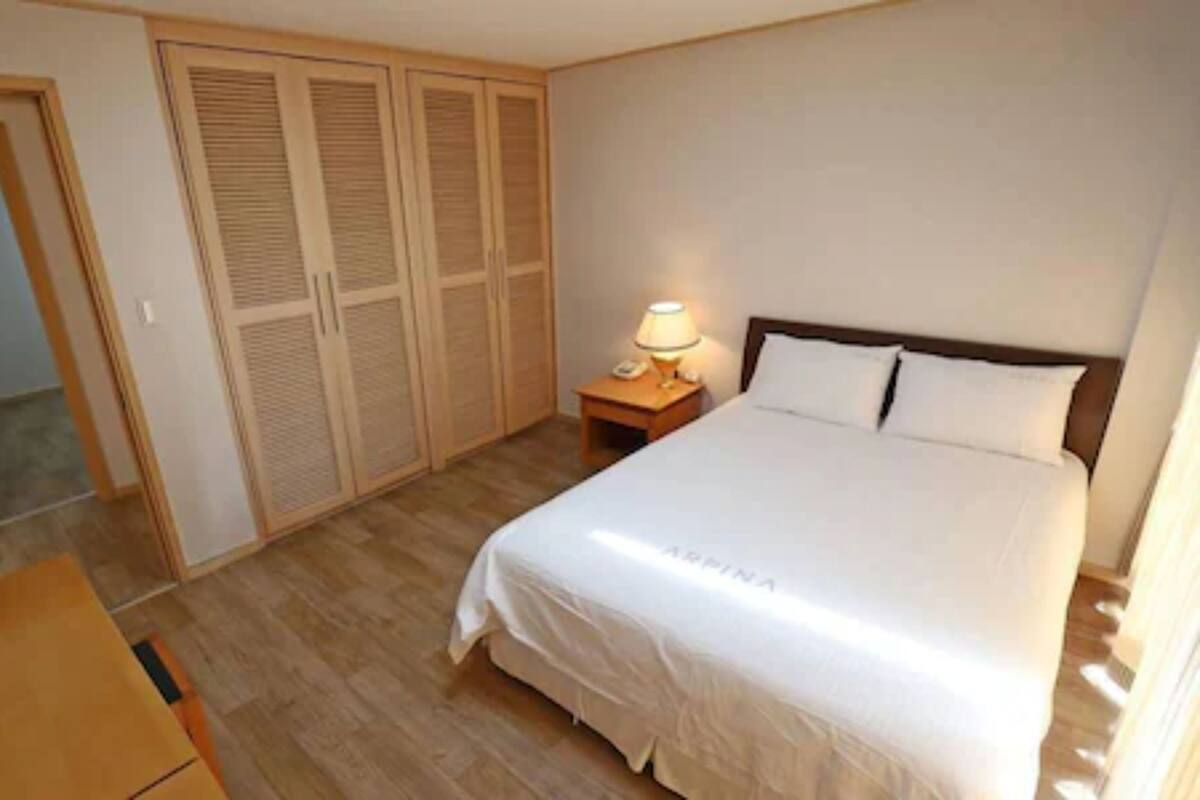 A bedroom with a bed, a nightstand with a lamp, and a wardrobe with louvered doors.