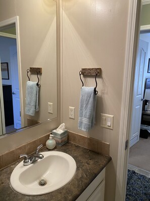 A bathroom with a white sink, a mirror, and two towels hanging on metal hooks.