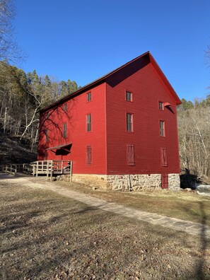 A red barn with a stone foundation, a wooden porch, and a dirt path leading to it. - Shawnee Creek Hideaway - Close to Eminence and the Jacks Fork River! (Eminence)