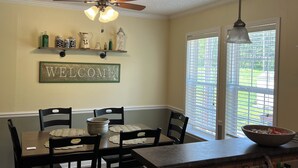 A dining area with a table set for four, a ceiling fan, and a 'WELCOME' sign on the wall. - Shawnee Creek Hideaway - Close to Eminence and the Jacks Fork River! (Winona)